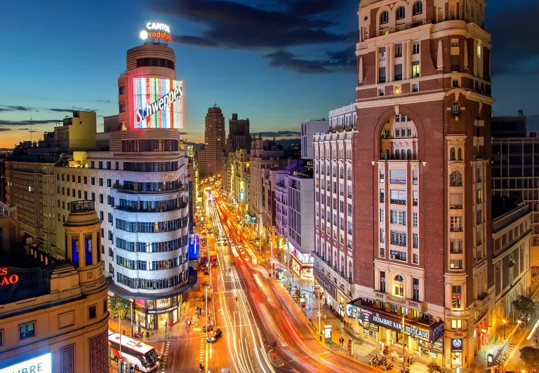 Nachtaufnahme der Gran Vía in Madrid mit ihrer lebendigen Architektur und dem geschäftigen Straßenleben.