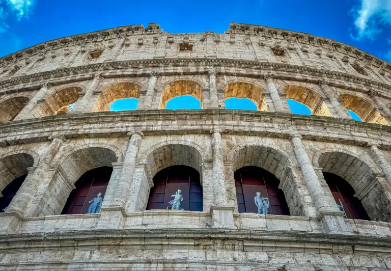 Low-angle view of the Colosseum in Rome, showcasing its impressive architecture and statues.