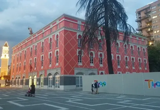Touristen erkunden ein leuchtend pinkes Gebäude und einen Uhrturm in Tirana, Albanien.