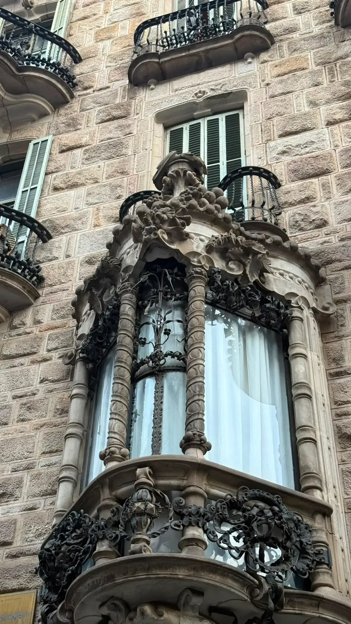 Ornate stone bay window and wrought iron balconies on the facade of a building in Barcelona.