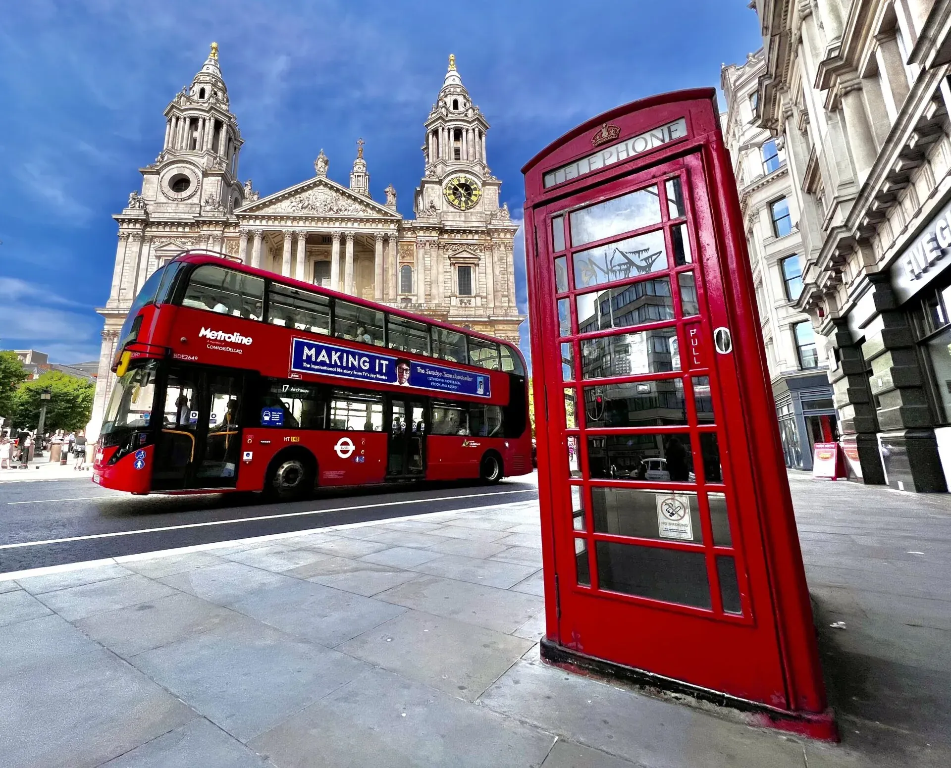 St Paul's Cathedral behind a red double-decker bus and a red telephone box on a sunny London street.