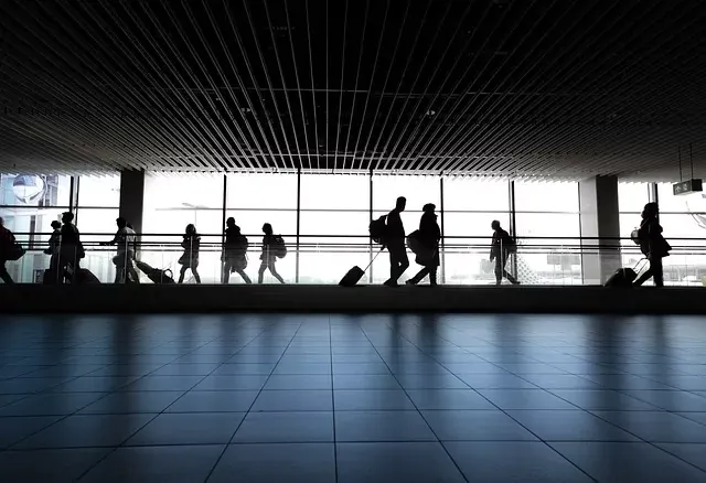 Silhouettes of passengers on a moving walkway in a modern airport terminal with large windows.