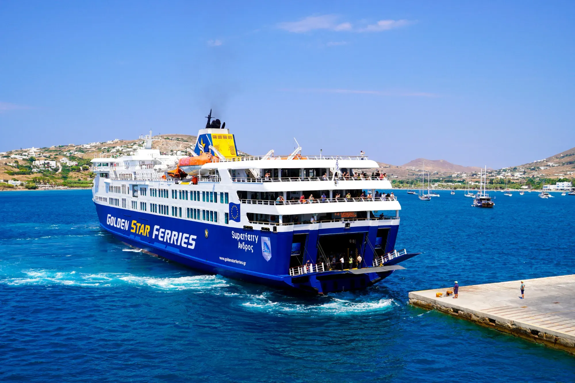 Ferry de pasajeros azul y blanco de Golden Star Ferries acercándose a un muelle de hormigón en una isla griega.