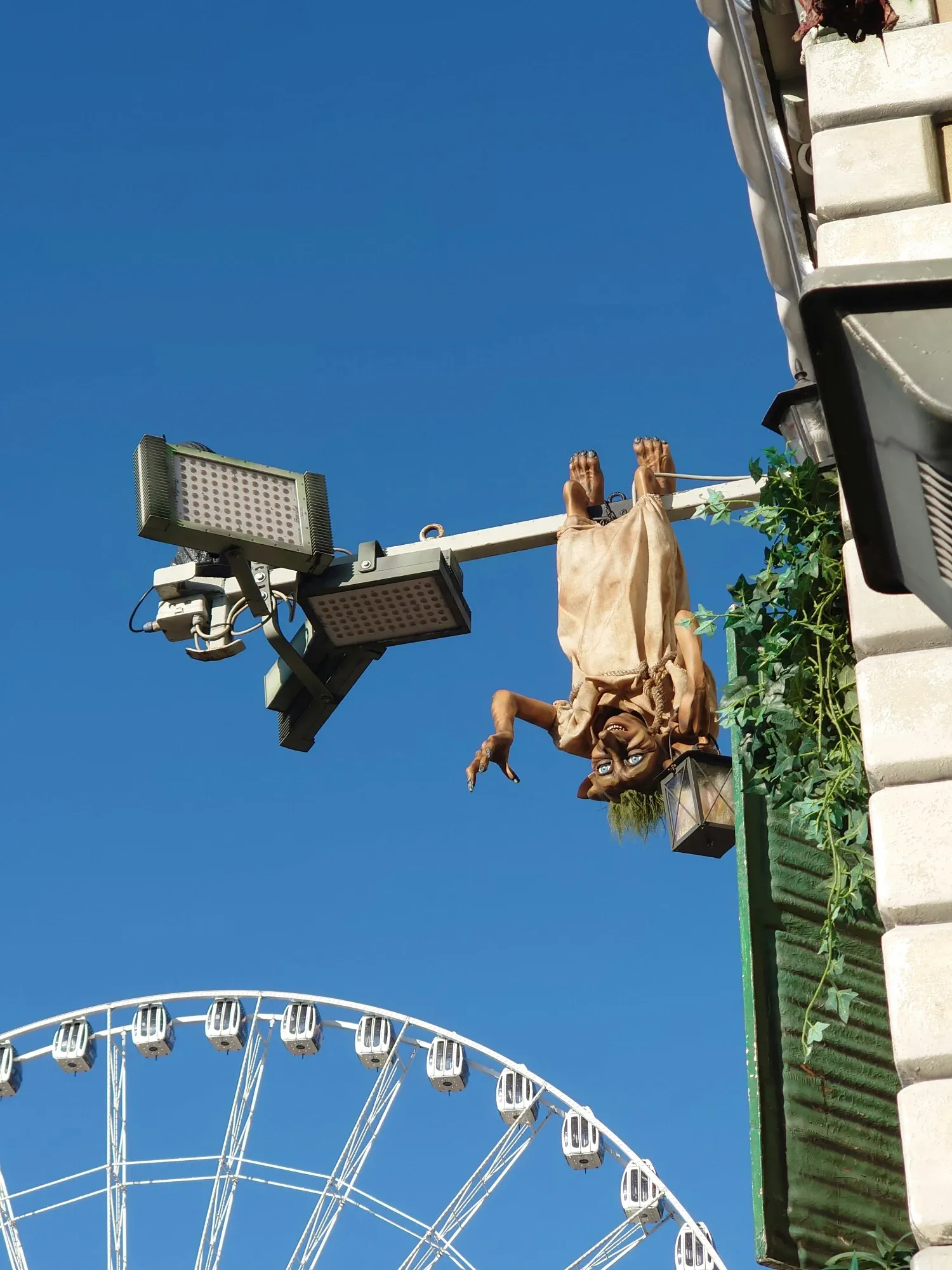 A goblin-like figure hangs upside down from a pole, holding a lantern, with a Ferris wheel in the background.