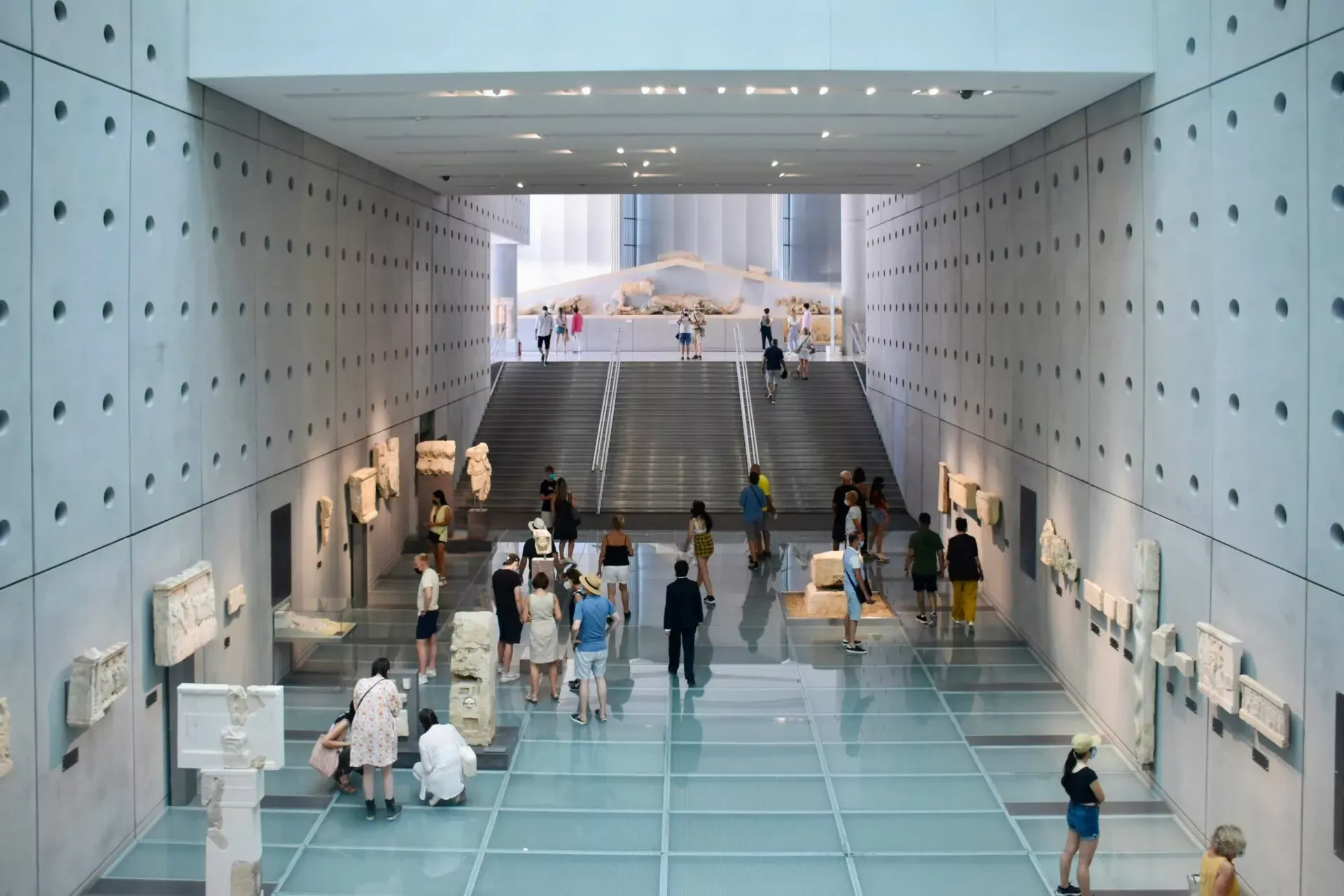 Modernes Museumsinterieur mit Glasboden über Ausgrabungen, Treppe und Ausstellung antiker griechischer Skulpturen und Friese.