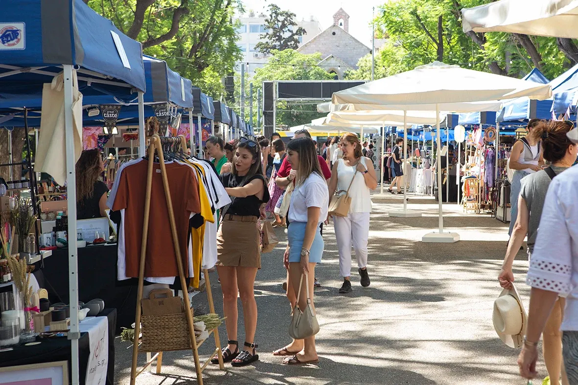 Menschen stöbern an Kleiderständen auf einem sonnigen Straßenmarkt in Athen.