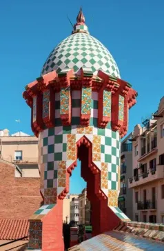 Una colorida chimenea del Palau Güell de Barcelona, con una cúpula a cuadros verdes y blancos y azulejos florales.