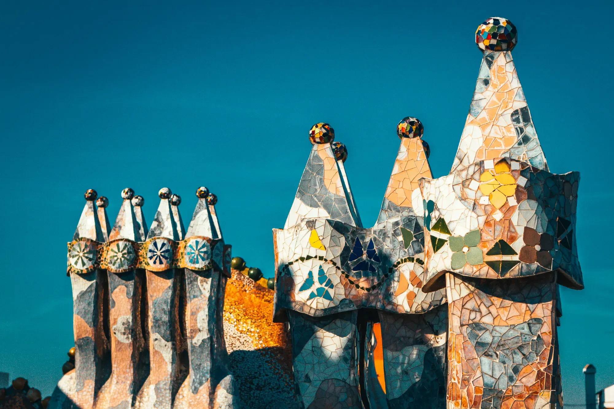 Colorful mosaic chimneys on the rooftop of Palau Güell in Barcelona against a clear blue sky.