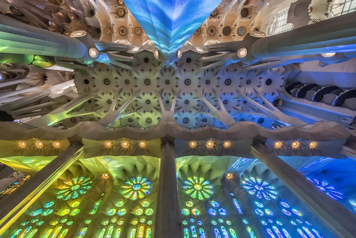 The intricate, colorful ceiling and stained glass windows of the Sagrada Familia in Barcelona, bathed in shifting light.