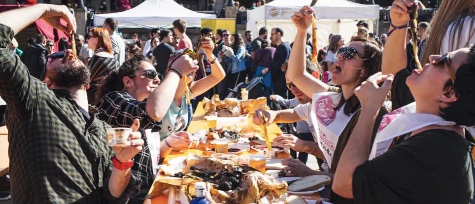 Menschen auf einem Calçotada-Fest in Barcelona essen gegrillte Calçots mit Lätzchen. Viele verkohlte Zwiebelschalen auf dem T