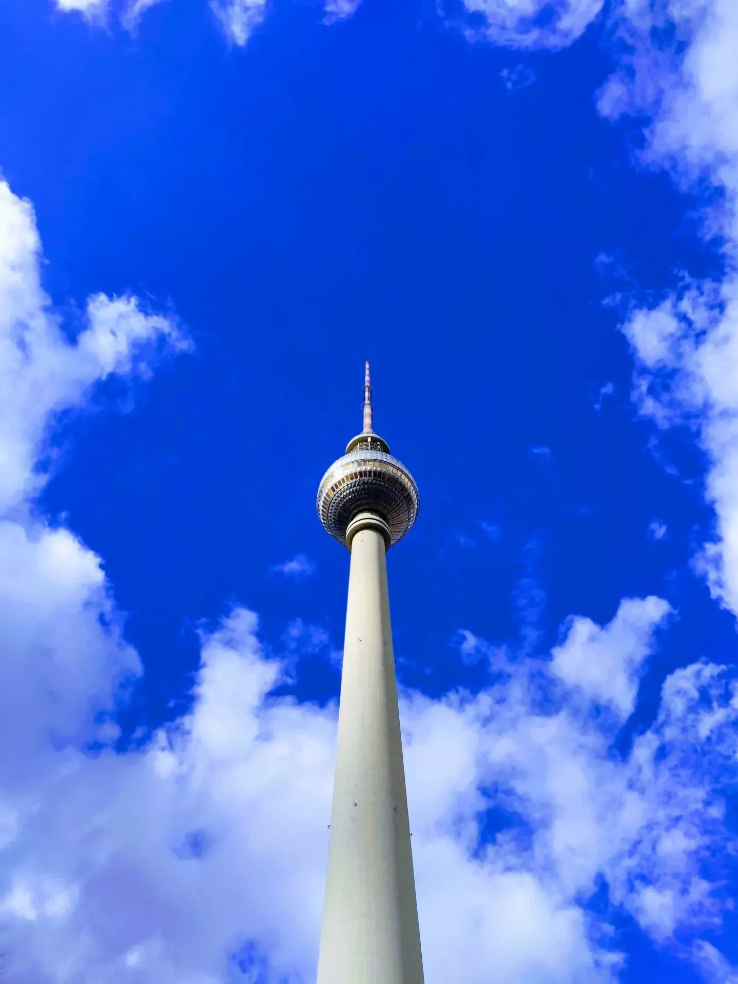 Der Berliner Fernsehturm von unten vor einem hellblauen Himmel mit vereinzelten weißen Wolken gesehen.