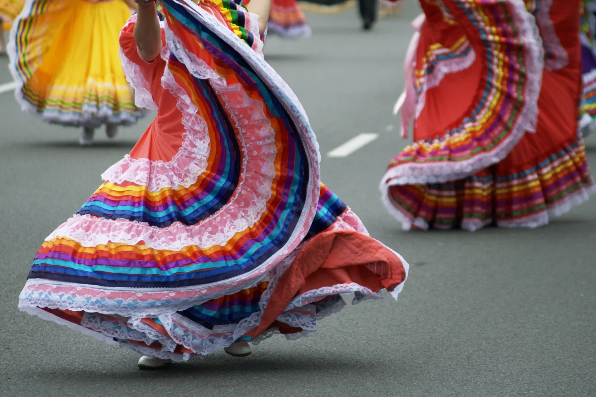 Bailarinas con vestidos coloridos de varias capas, cintas de arcoíris y encajes blancos durante un desfile callejero.