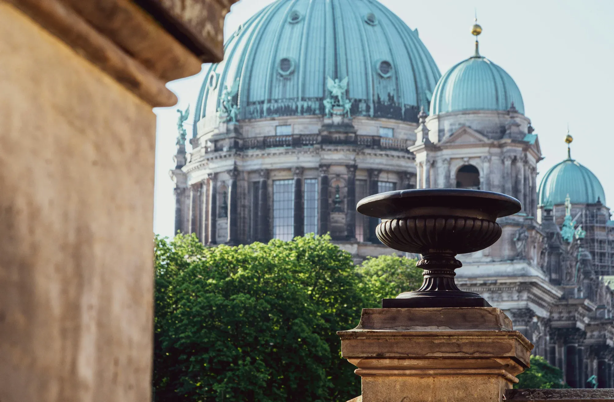 Las cúpulas turquesas de la Catedral de Berlín vistas desde un balcón de piedra, con una urna en primer plano.