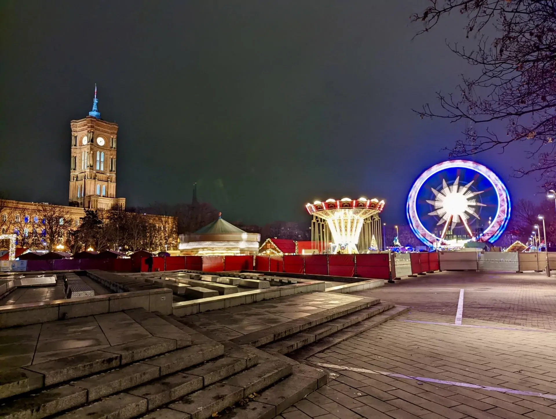 Vista nocturna de una noria, carrusel y puestos de mercado con la torre del reloj del Rotes Rathaus iluminada en Berlín.