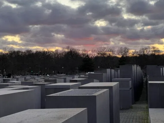 Betonowe stele Pomnika Pomordowanych Żydów Europy w Berlinie pod zachmurzonym wieczornym niebem.