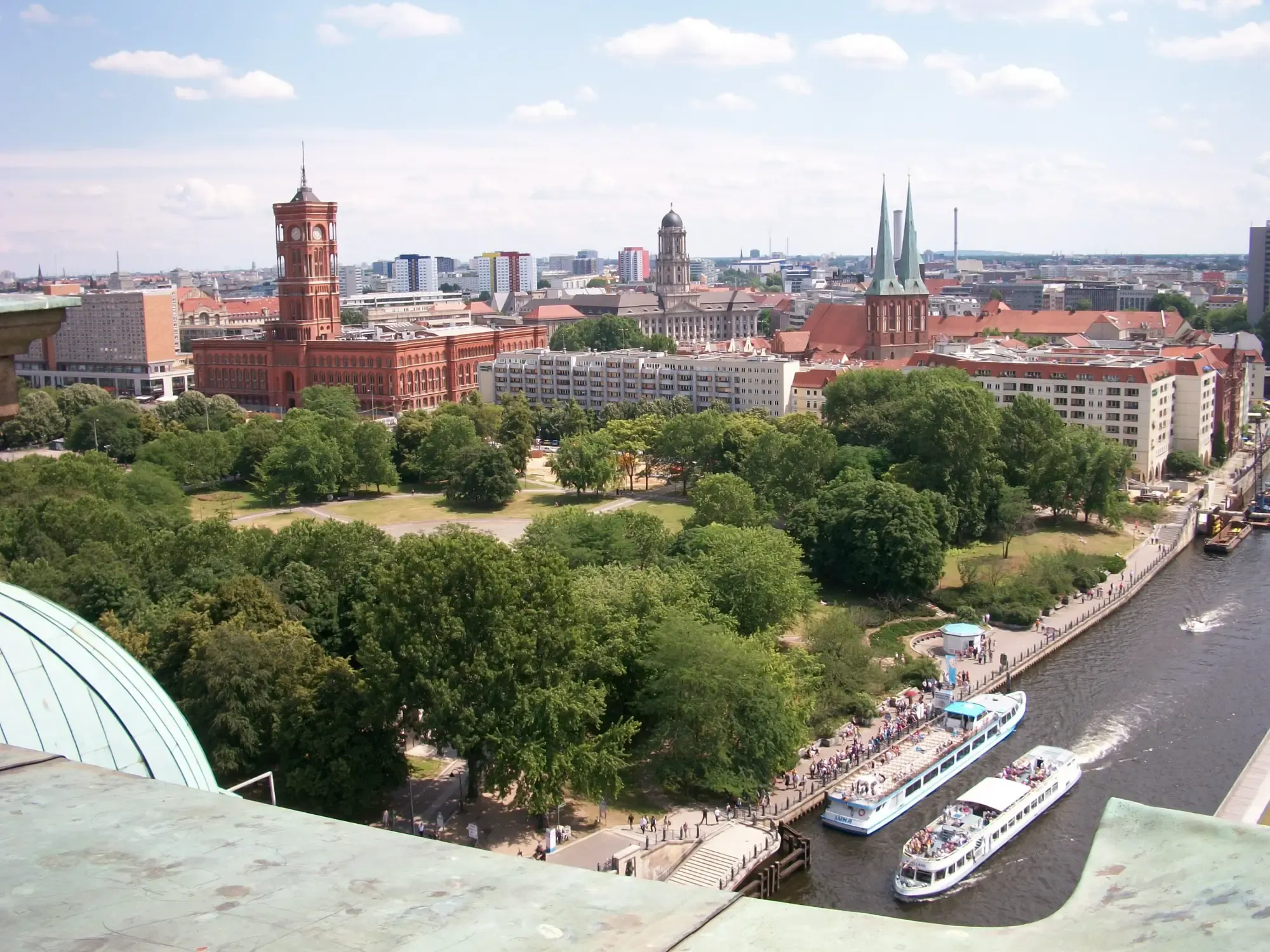 Luftaufnahme des Berliner Stadtzentrums mit dem roten Roten Rathaus, Bäumen, der Spree und Ausflugsbooten.