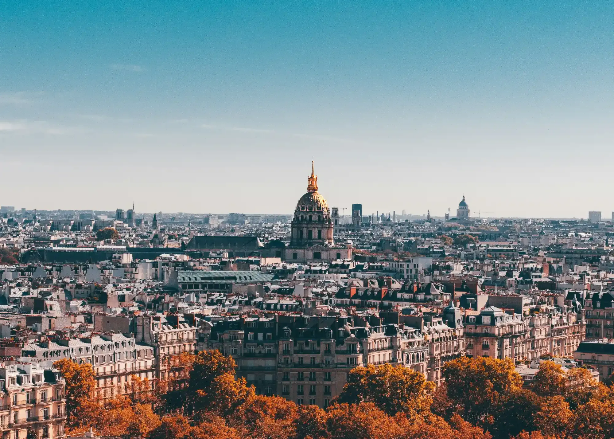Paris skyline with the golden dome of Les Invalides in the centre, seen on a clear day with autumn trees in the foreground.