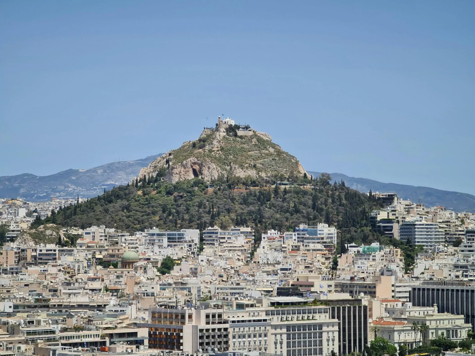 Panoramiczny widok na Ateny z Wzgórzem Lykabettus i białą kaplicą na szczycie, pod czystym niebem.