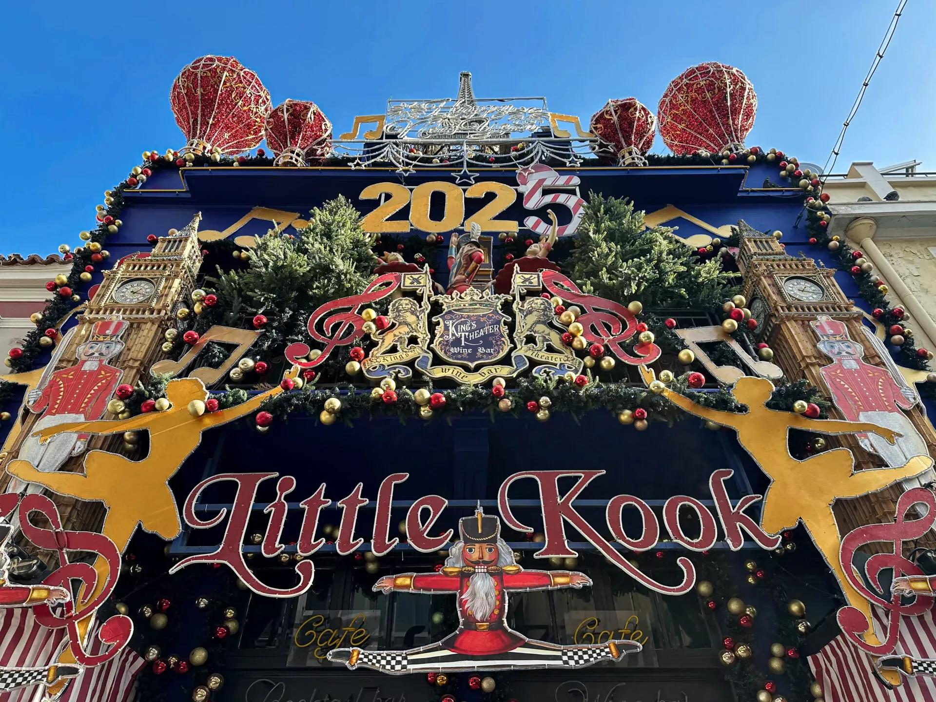 Elaborately decorated cafe facade for 'Little Kook' with '2025', nutcrackers, clocks, hot air balloons, and festive garlands.