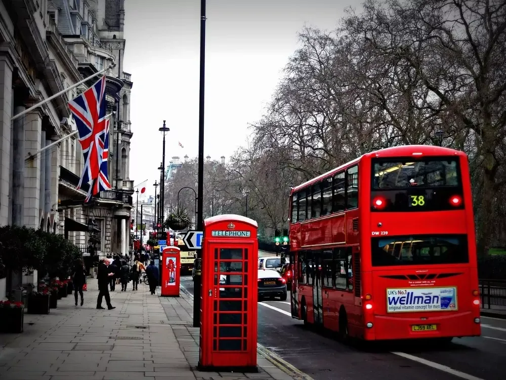 Autobús rojo de dos pisos en una calle junto a una cabina telefónica roja y un edificio con la bandera Union Jack en Londres.