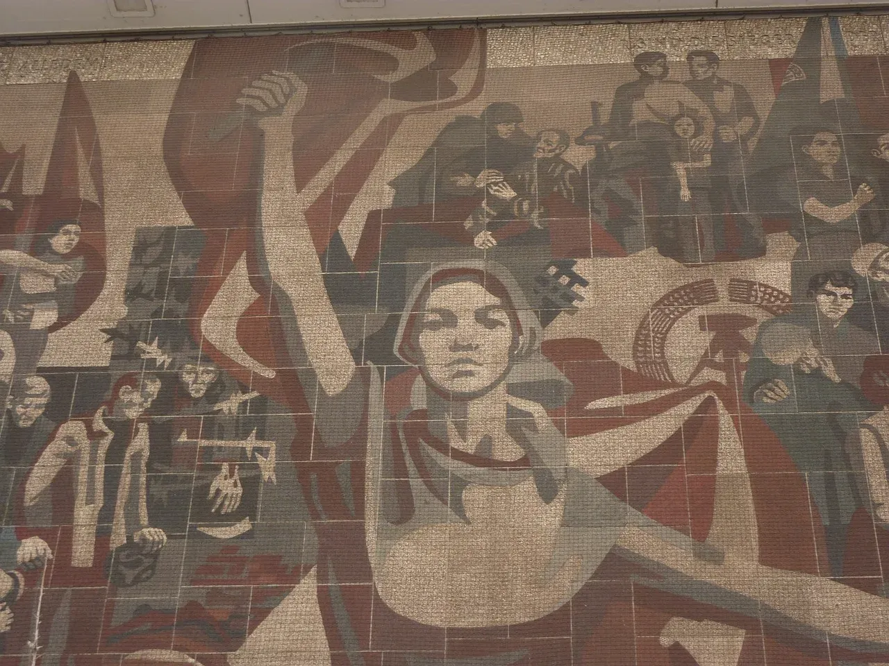 Gran mural de mosaico realista-socialista en tonos rojos, grises y beige, que representa trabajadores, banderas y una figu...