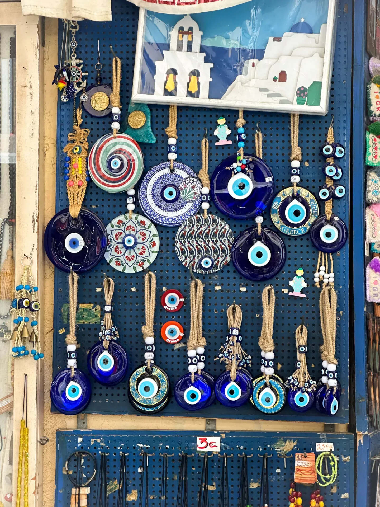 Display board showing many blue and white evil eye amulets of various sizes and patterns hanging on twine loops in a souvenir