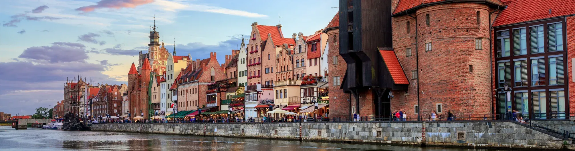 Panoramic view of historic red-roofed buildings lining the Motława River in Gdańsk, including the Żuraw Crane.