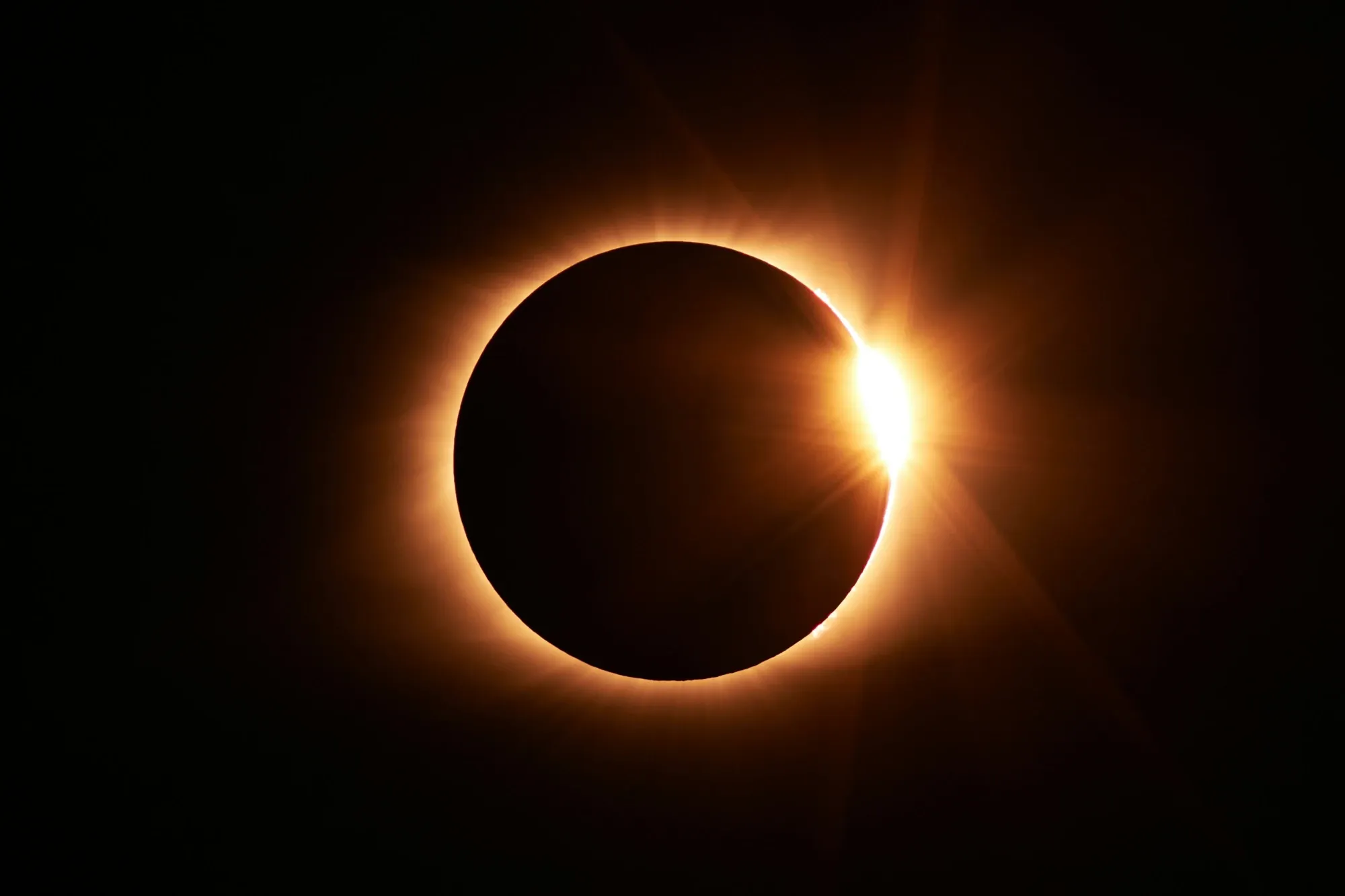 La luna oculta al sol durante un eclipse solar total, con la corona solar visible como un brillante anillo de luz.