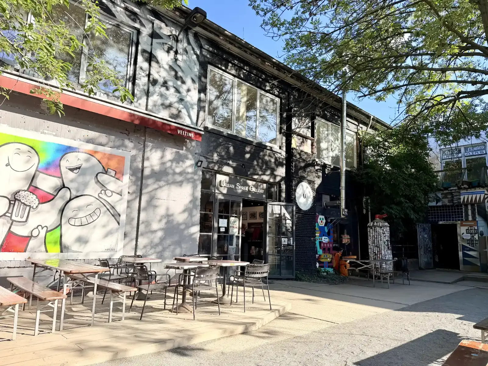Courtyard of the Urban Spree Gallery in Berlin, with street art, outdoor tables, and the gallery entrance.
