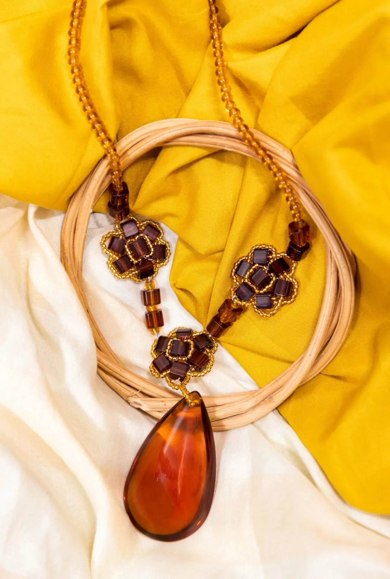 Amber bead necklace with a large teardrop pendant and decorative floral elements, resting on cream and yellow fabric next to