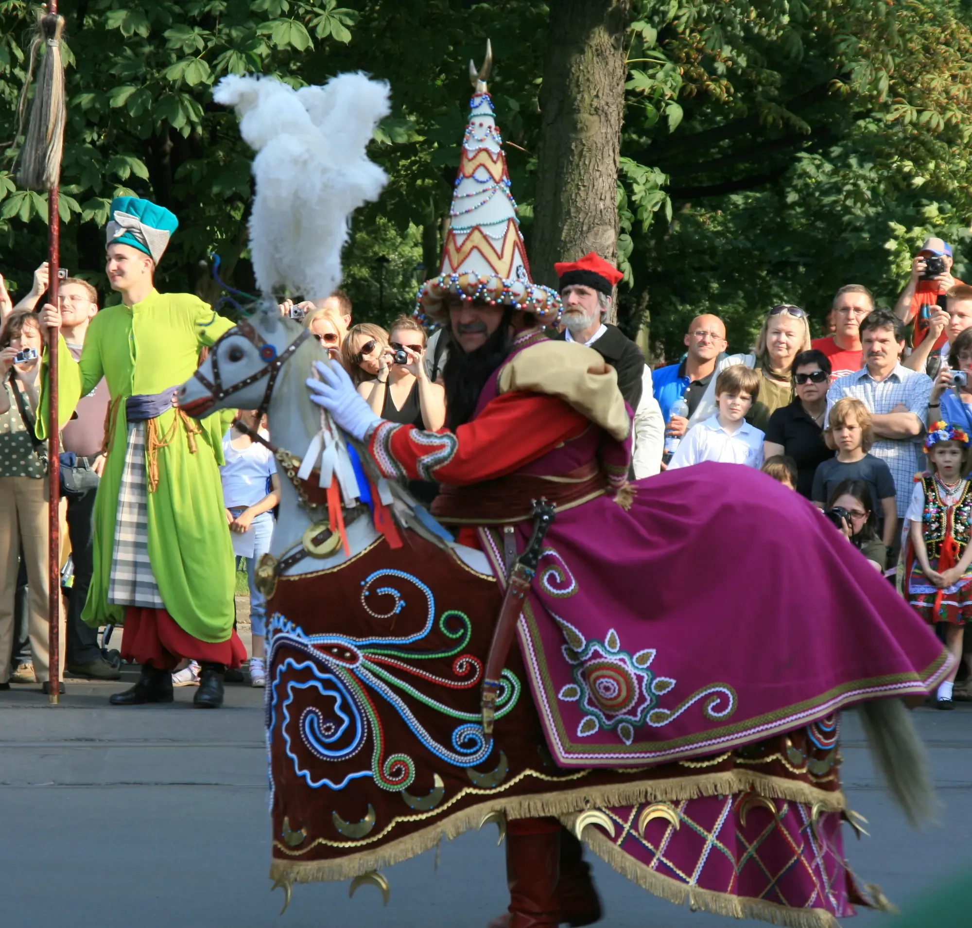 A man in the colourful Lajkonik costume, a hobby horse with a pointed hat, at a parade in Krakow surrounded by onlookers.