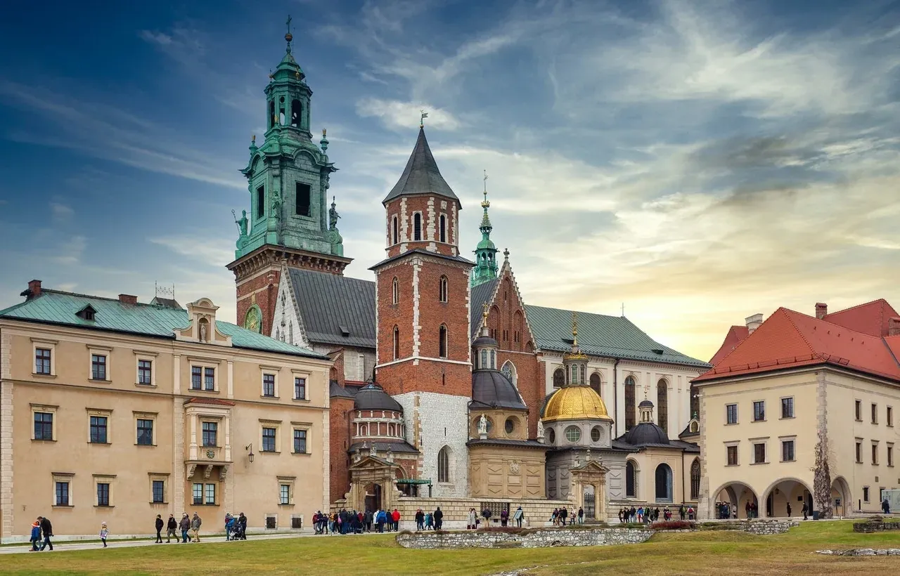 El complejo de la Catedral de Wawel en un día parcialmente nublado, con sus diversas torres y capillas vistas desde el césped