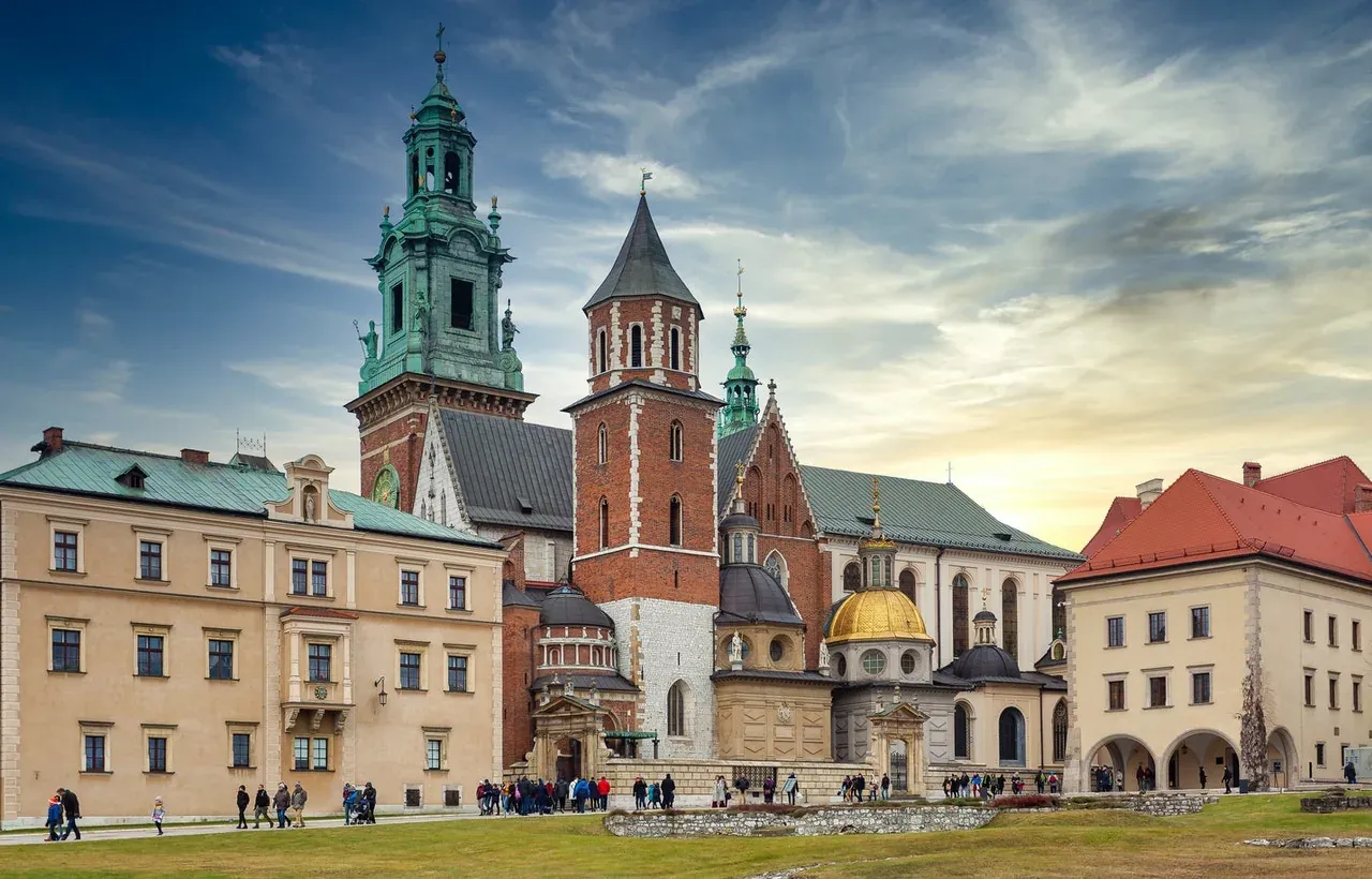 Arquitectura histórica de la Catedral de Wawel con techos verdes, torres de ladrillo y cúpula dorada, bajo cielo parcialmente