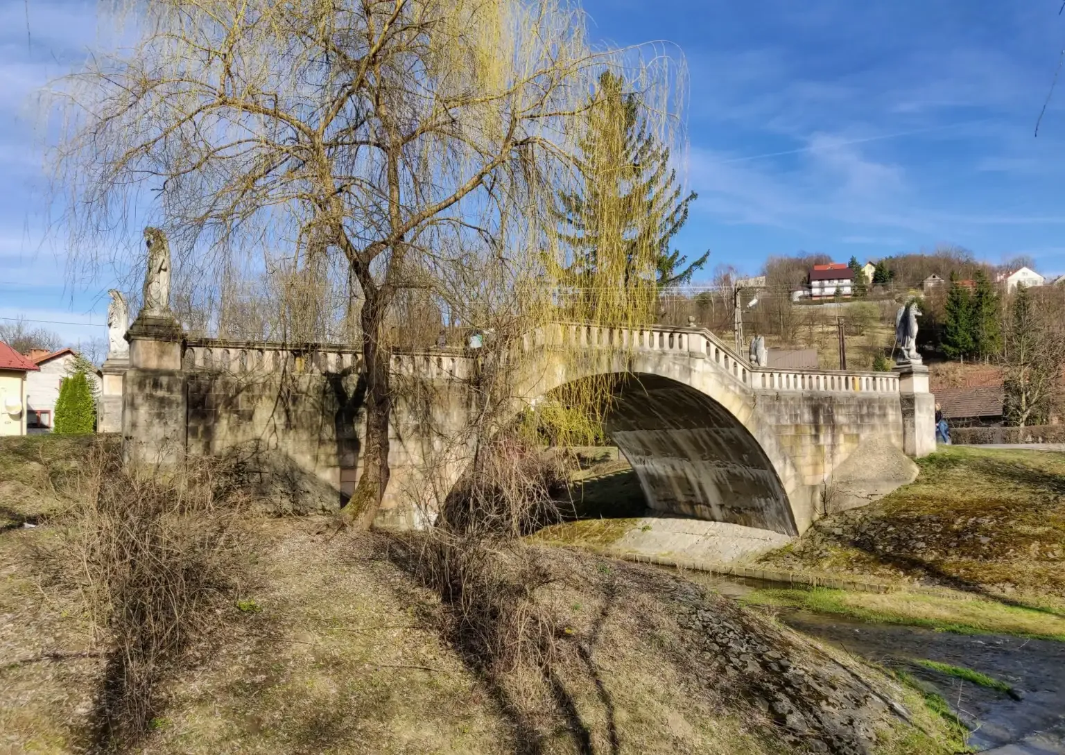 El histórico puente de arco de piedra de los Ángeles en Lanckorona, Polonia, en un día soleado con un sauce en primer plano.