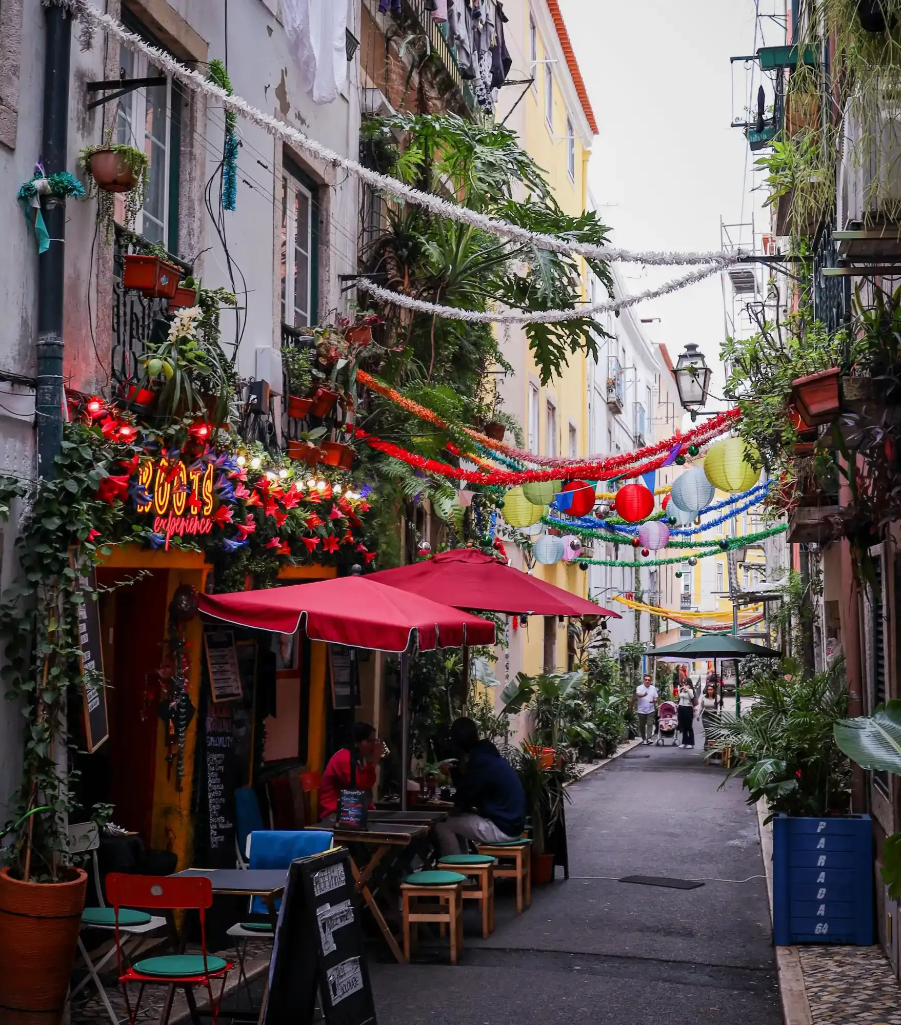 Narrow Lisbon street lined with cafes, plants, and colourful decorations strung between the residential buildings.