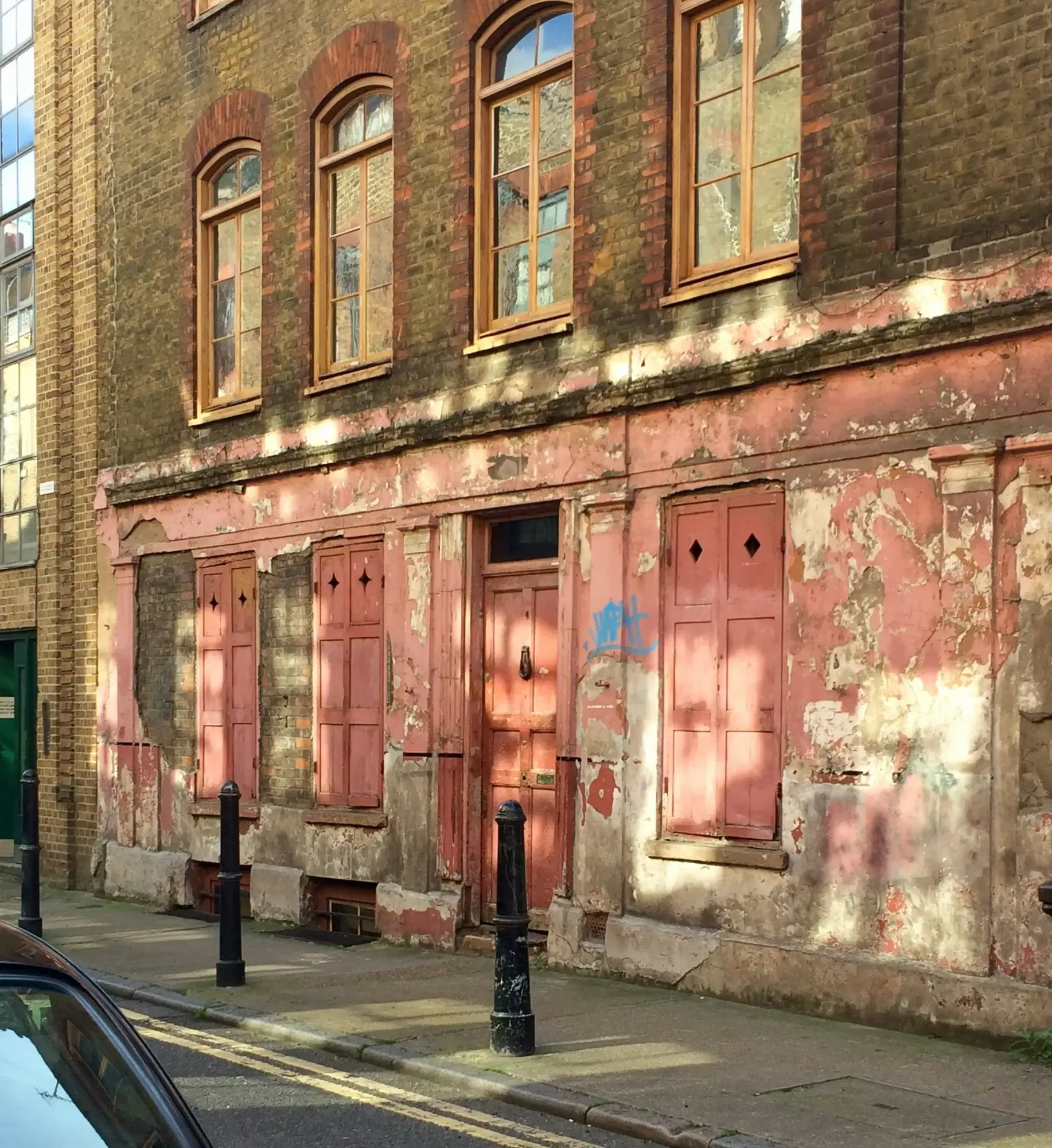 Ein verwittertes Backsteingebäude mit einer verblassten rosa Ladenfront im Erdgeschoss, gesehen von einer Londoner Straße ...