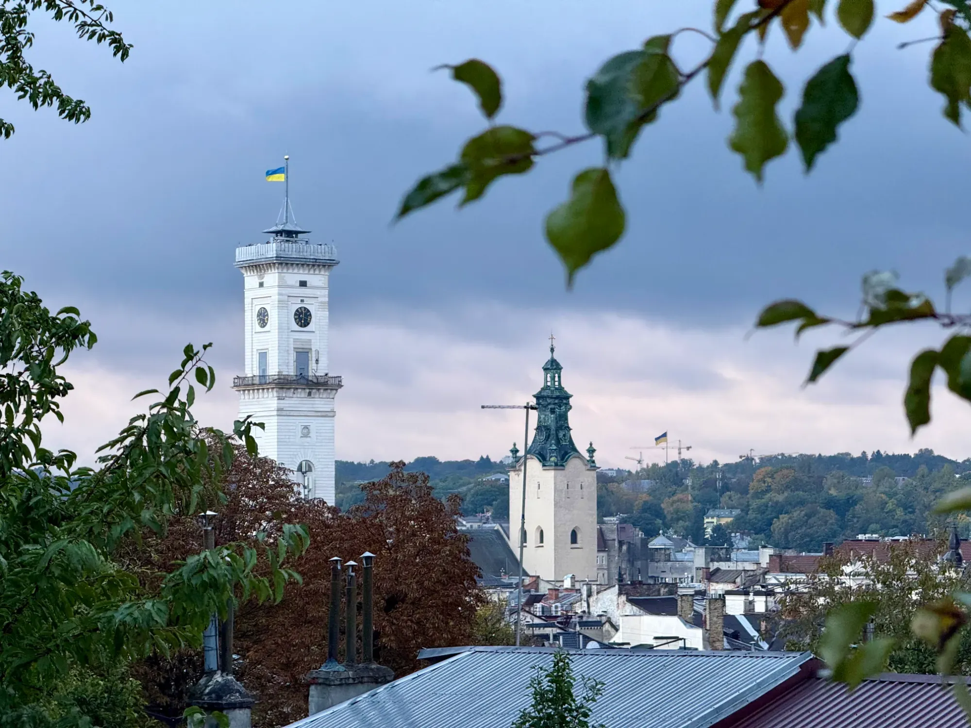 View of Lviv's skyline with the white Town Hall clock tower flying a Ukrainian flag, and the Latin Cathedral spire.