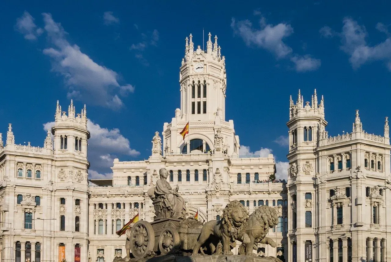 Cibeles Fountain with a seated goddess in a chariot pulled by two lions, in front of the ornate Palacio de Cibeles in Madrid.