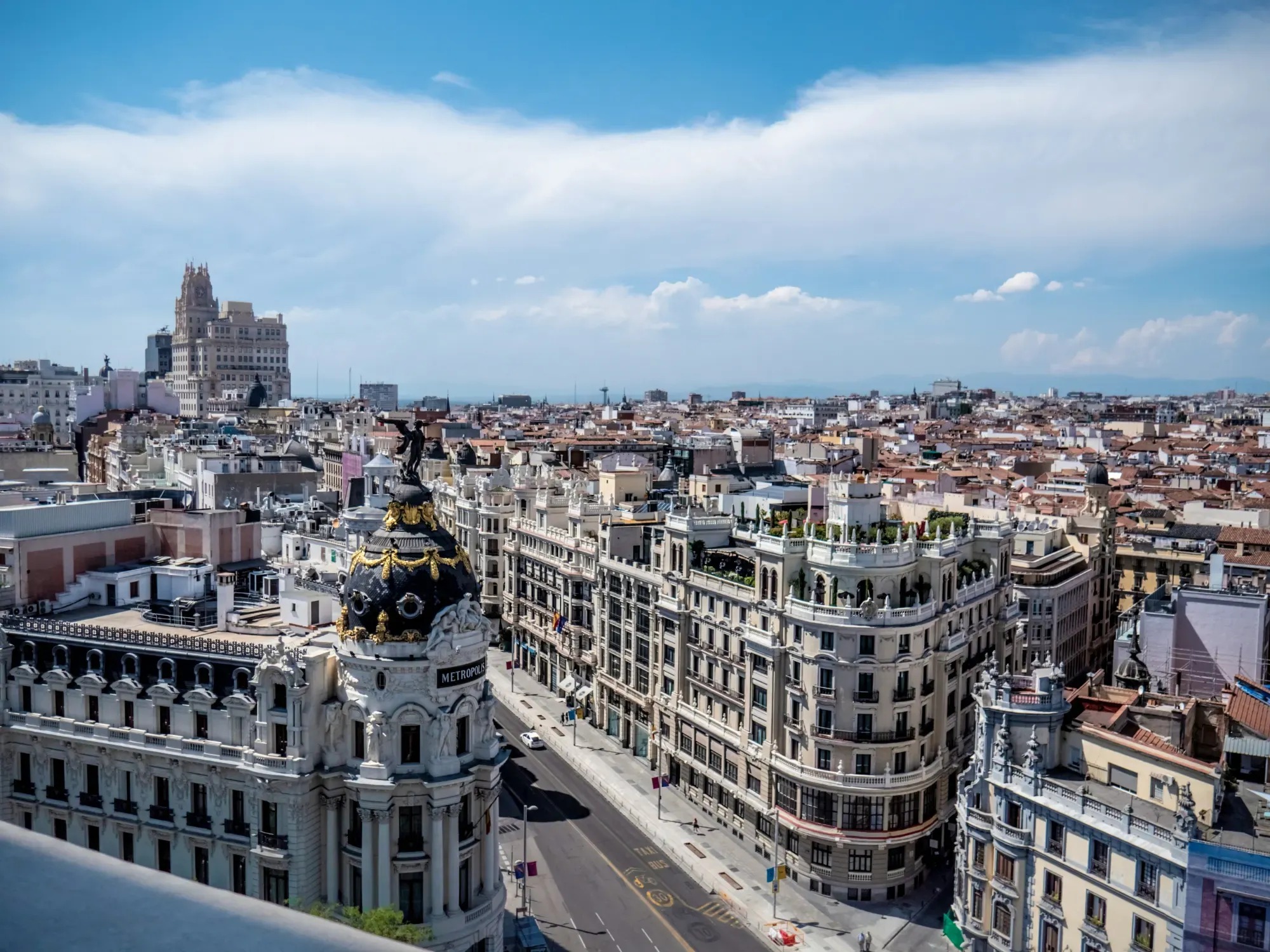 Aerial view of Madrid's Gran Vía street, featuring the Metropolis Building and surrounding historic architecture under a blue