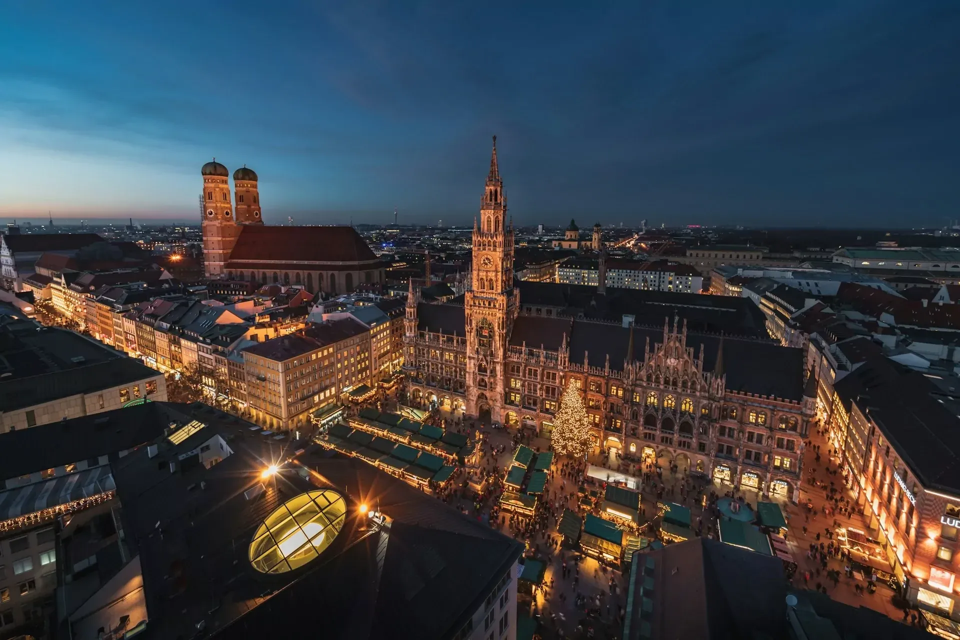 Luftaufnahme von Münchens Marienplatz bei Nacht während des Weihnachtsmarktes. Neues Rathaus und Frauenkirche sind unter blau
