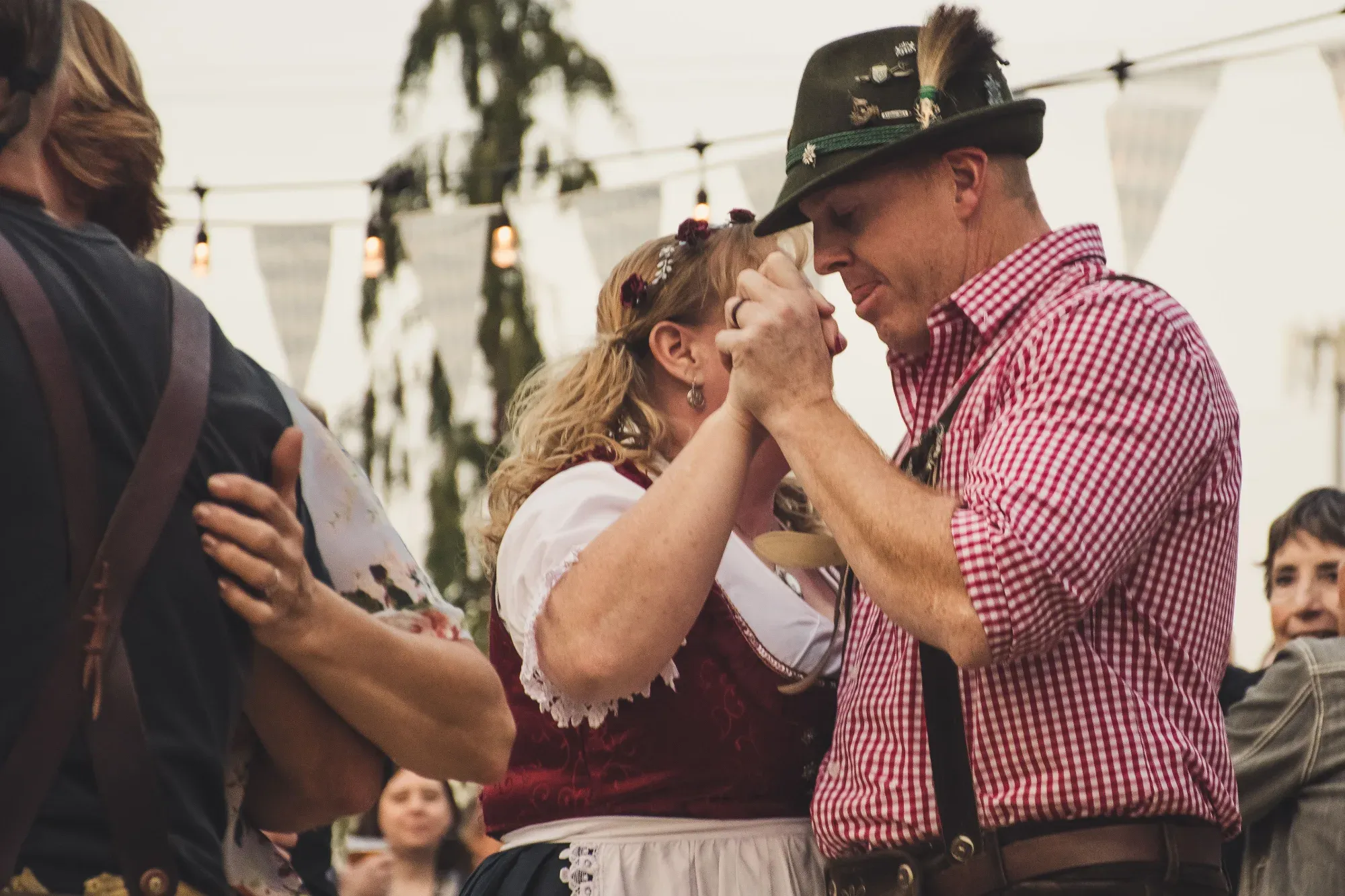 A man and woman in traditional Bavarian attire, including a dirndl and a feathered hat, dance closely together.