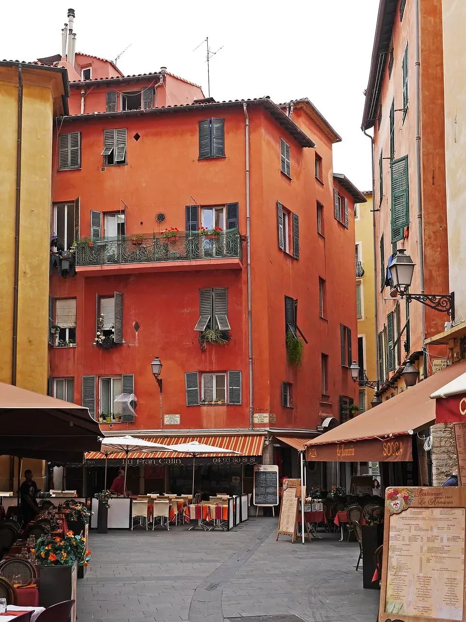 Narrow street in Nice Old Town with terracotta buildings, open shutters, and several restaurants offering outdoor seating und