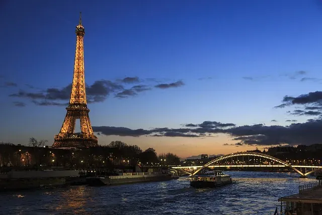 Beleuchteter Eiffelturm und Brücke Pont de Bir-Hakeim bei Dämmerung, mit Booten auf der Seine in Paris.
