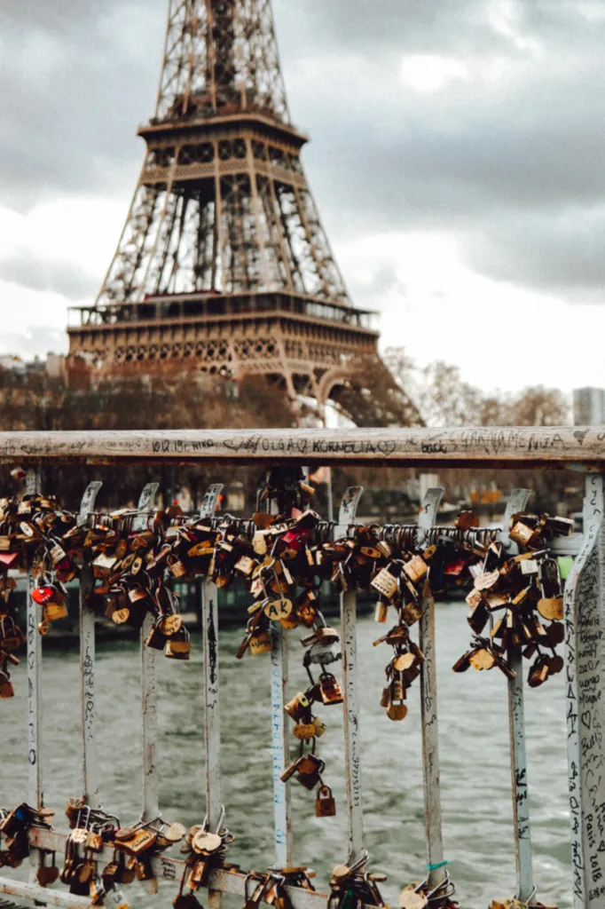 Love padlocks attached to a bridge railing with the blurred Eiffel Tower in the background in Paris.