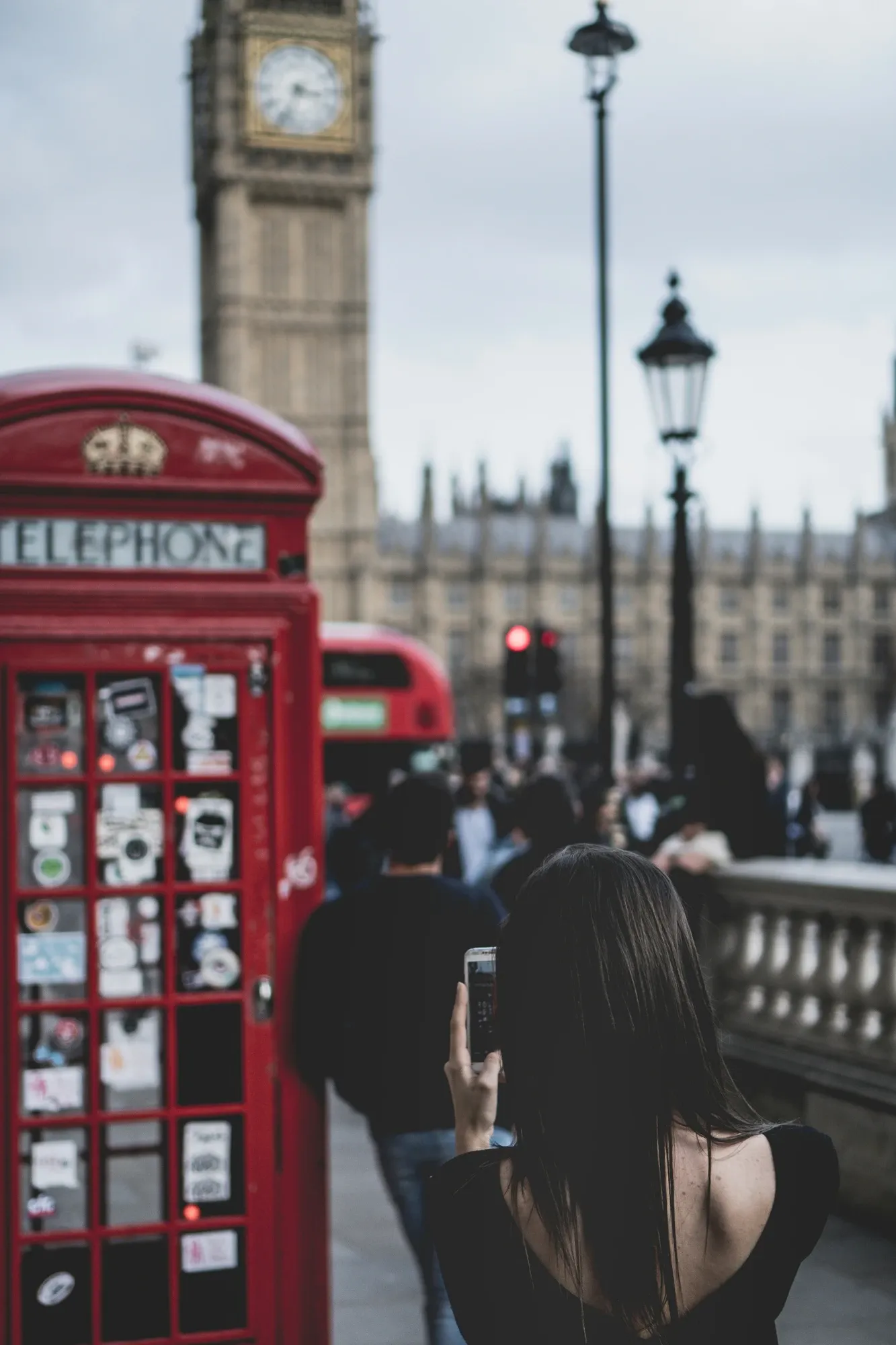 Kobieta fotografuje czerwoną budkę telefoniczną, z rozmytą w tle Wieżą Elżbiety (Big Ben) i budynkiem Parlamentu.