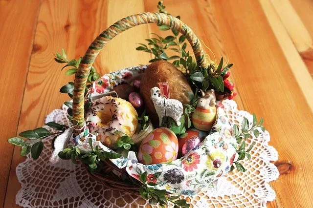 A traditional Polish Easter basket (Święconka) filled with bread, a donut, decorated eggs, chocolate, lamb, and sprigs on a d