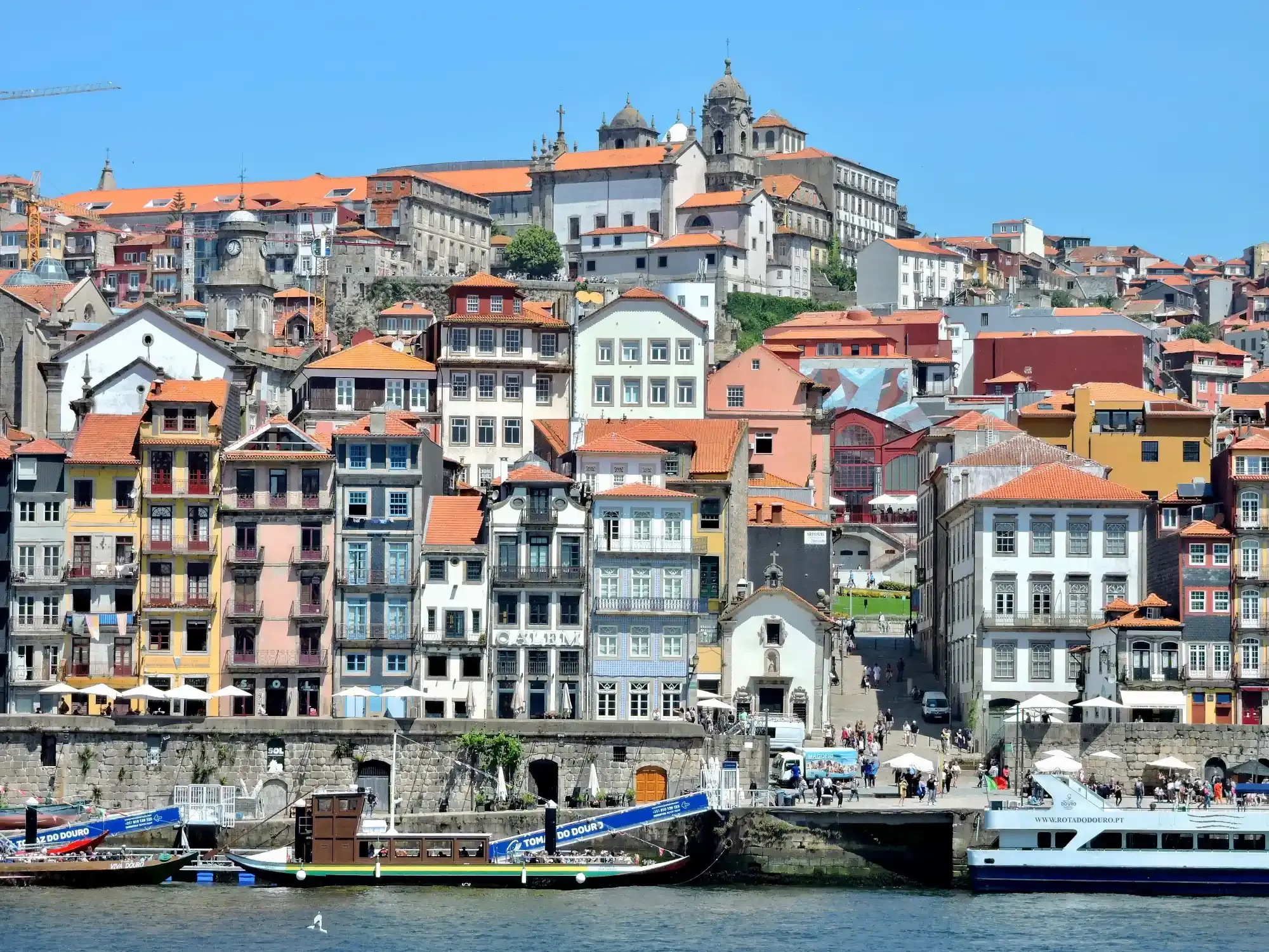 Bunte historische Gebäude des Ribeira-Viertels in Porto ragen über dem Fluss Douro auf, darunter liegen Touristenboote vor...