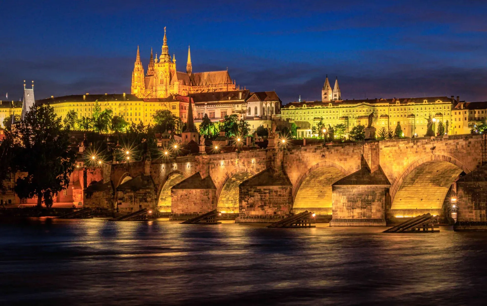 El Puente de Carlos y el Castillo de Praga iluminados al anochecer, con el río Moldava reflejando luces.