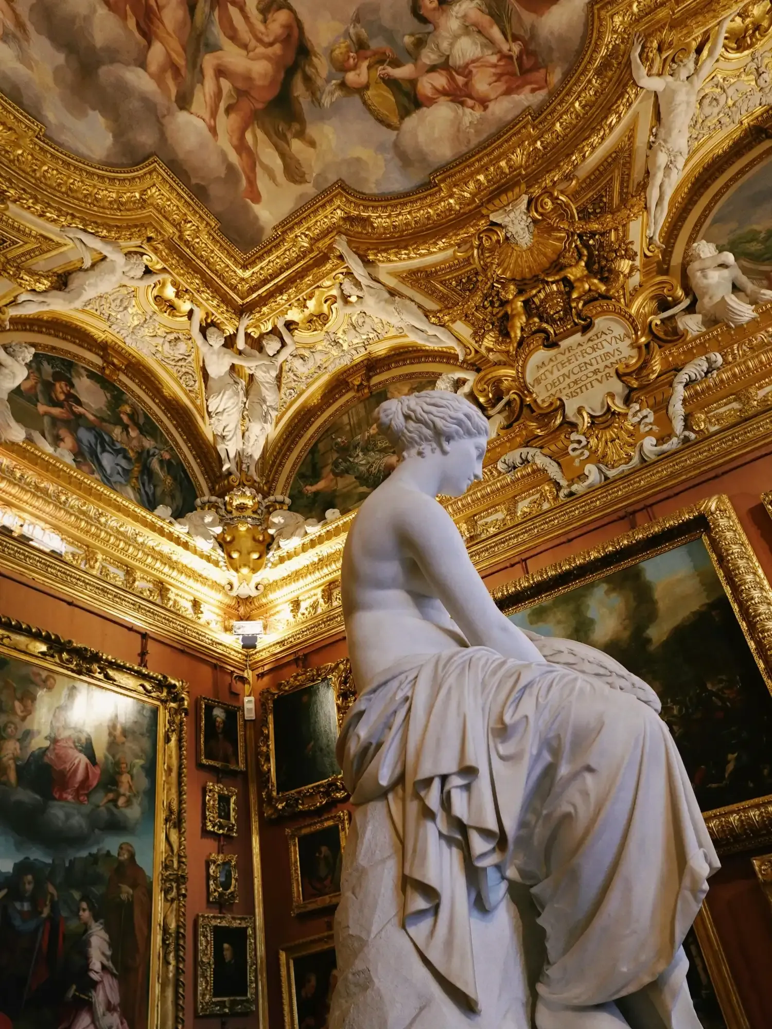 Una estatua de mármol de una mujer en una opulenta galería con techo dorado, pinturas y estucos.