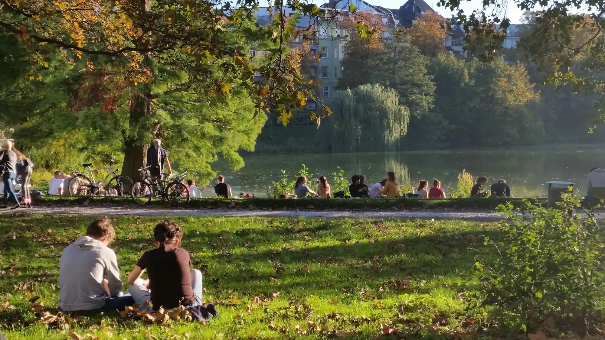 People relaxing on a grassy bank by a lake in a Berlin park on a sunny afternoon.